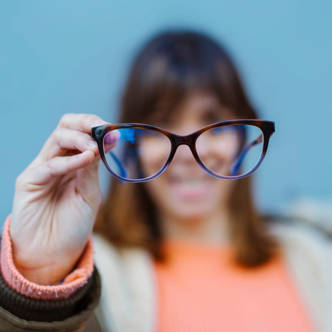 Young lady holding designer eyeglasses in the foreground with a blurred background
